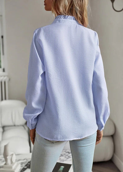 Femme portant une chemise bleue texturée, manches longues, dans un salon moderne. Mode féminine, tenue décontractée, style élégant.