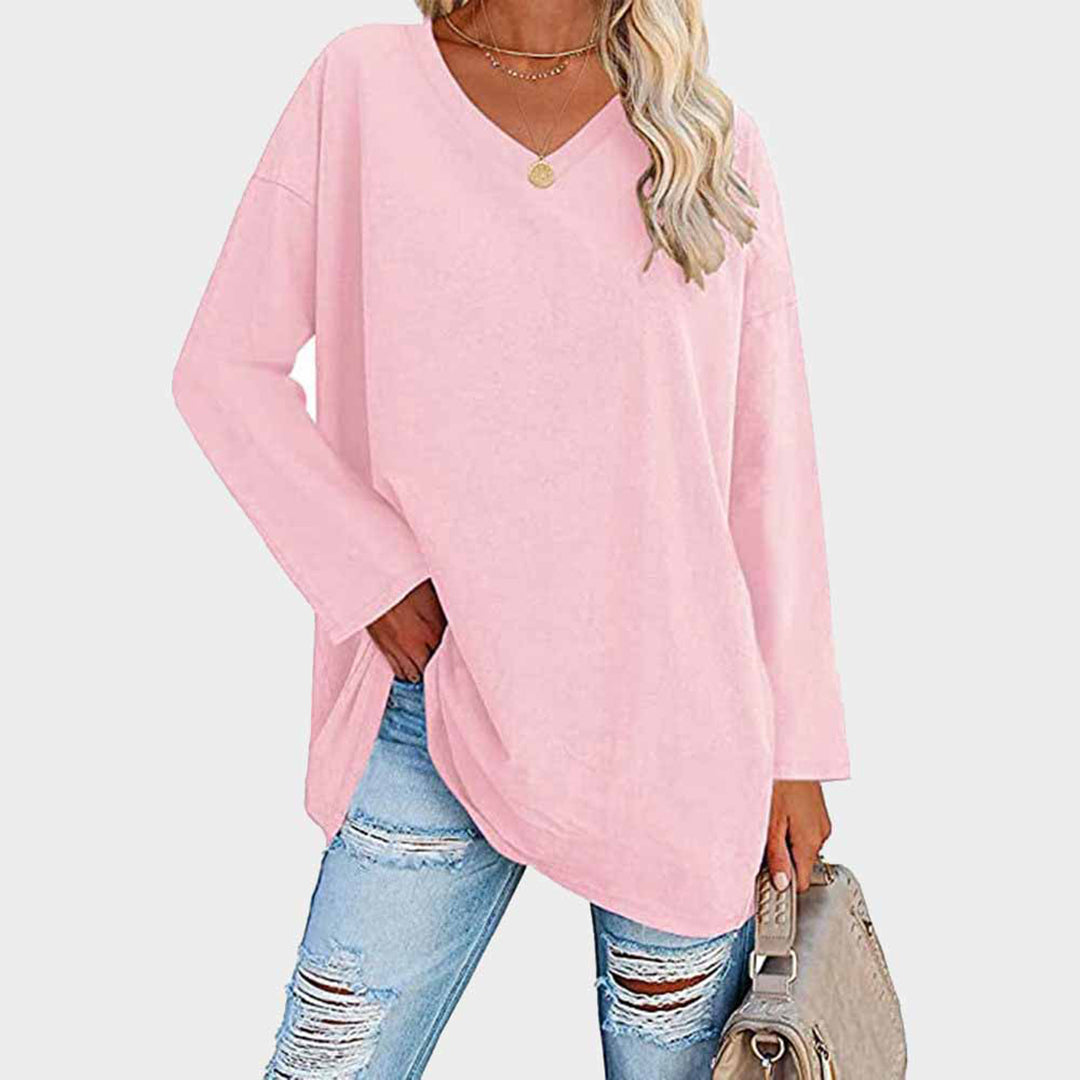 Femme portant un pull rose ample à col en V, associé à un jean déchiré bleu clair et un sac à main beige. Mode décontractée tendance.