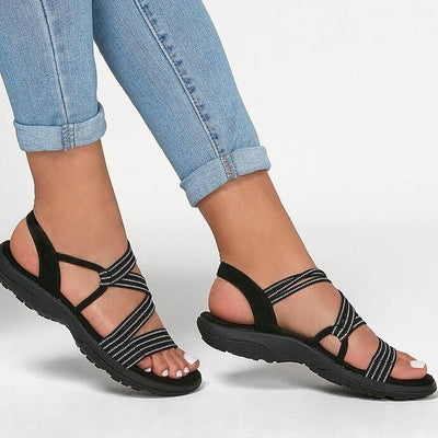 Sandales noires à brides croisées pour femme, portées avec un jean bleu clair. Chaussures d'été confortables et élégantes, semelle antidérapante.