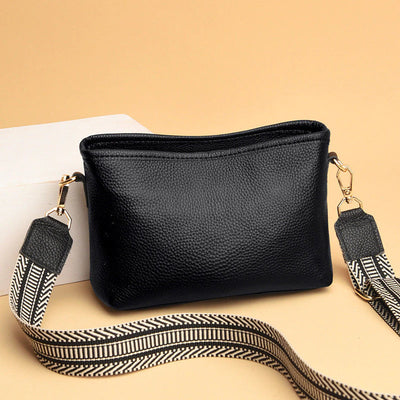 Sac à bandoulière noir en cuir texturé avec sangle ajustable à motifs géométriques, posé sur fond beige. Accessoire mode élégant et pratique.