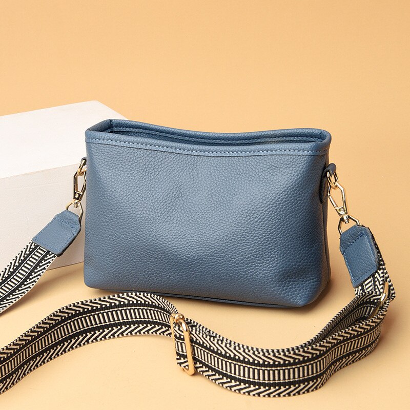 Sac à main en cuir bleu avec bandoulière à motif zigzag noir et blanc, posé sur fond beige. Accessoire mode élégant et tendance.