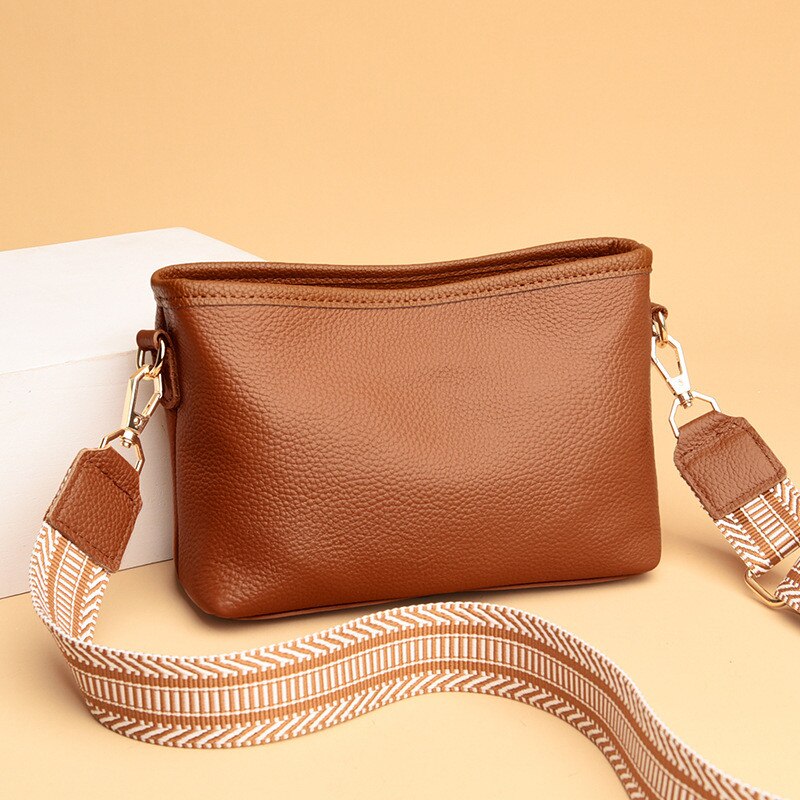 Sac à main en cuir marron avec bandoulière amovible à motifs géométriques, posé sur fond beige. Accessoire mode élégant et tendance.