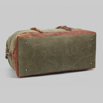 Sac de voyage en toile verte et cuir marron, base renforcée, rivets métalliques, poignées robustes. Accessoire de mode durable et élégant.