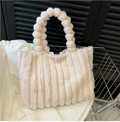 Sac à main en fausse fourrure beige avec anses perlées, posé sur un fond moderne. Accessoire tendance, élégant et doux pour l'hiver.