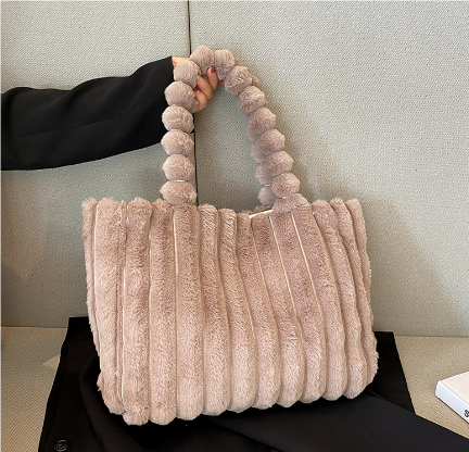 Sac à main en fausse fourrure beige avec anses texturées, posé sur un fond neutre. Accessoire mode tendance, élégant et doux au toucher.