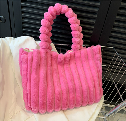 Sac à main rose en fausse fourrure avec anse perlée, posé sur un tissu blanc. Accessoire tendance, mode féminine, design élégant.