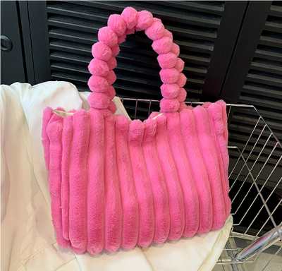 Sac à main rose en fausse fourrure avec anse perlée, posé sur un tissu blanc. Accessoire tendance, mode féminine, design élégant.