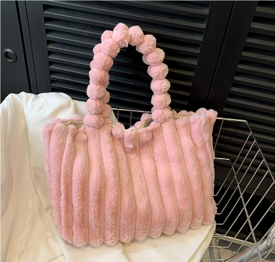 Sac à main rose en fausse fourrure avec anses perlées, posé sur un tissu blanc. Accessoire mode tendance, élégant et doux pour l'hiver.