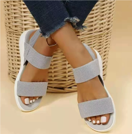 Sandales grises en tissu sur pieds féminins, posées sur un panier en osier. Chaussures d'été confortables, style décontracté, mode féminine.