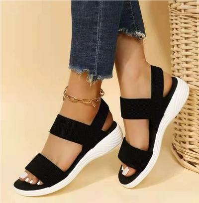 Sandales noires à semelles blanches portées avec un jean déchiré, posées près d'un panier en osier. Mode estivale, chaussures confortables.