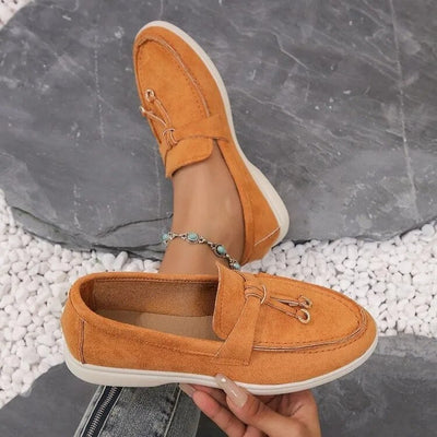 Chaussures mocassins en daim orange pour femme, posées sur des galets blancs. Élégantes et confortables, idéales pour un style décontracté.