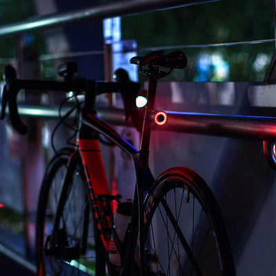 Vélo de route noir avec feux arrière LED rouges, stationné sur un pont la nuit. Éclairage urbain, cyclisme nocturne, sécurité vélo.