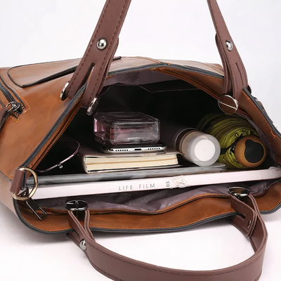 Sac à main en cuir marron ouvert, contenant un livre, des lunettes de soleil, un parfum, un parapluie et un carnet. Accessoires de mode élégants.