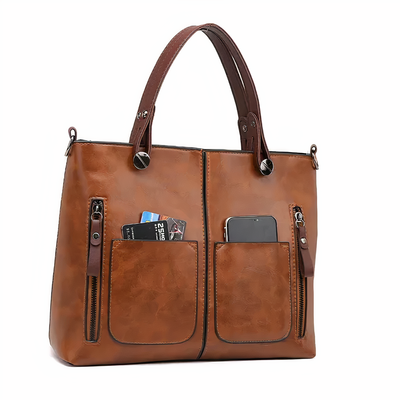 Sac à main en cuir marron avec poches avant zippées, contenant un smartphone et des cartes. Élégant et pratique pour un usage quotidien.