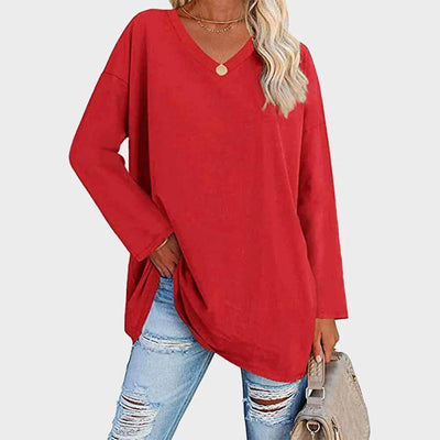 Femme portant un pull rouge ample à col en V, associé à un jean déchiré et un sac beige. Mode décontractée, tendance automne-hiver.