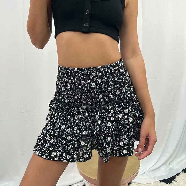 Femme en jupe fleurie noire et blanche, top court noir, posant devant un fond blanc. Mode estivale, tenue décontractée, style tendance.