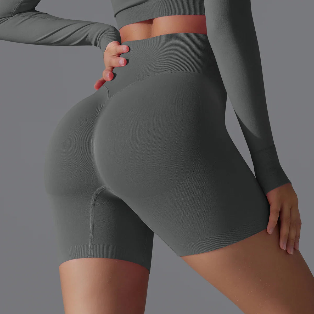 Femme en tenue de sport grise moulante, mettant en valeur des shorts taille haute. Mode fitness, vêtements de sport, style athlétique moderne.