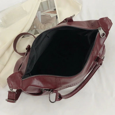 Sac à main en cuir bordeaux ouvert, intérieur noir, avec bandoulière réglable et fermetures éclair argentées, posé sur un fond blanc.