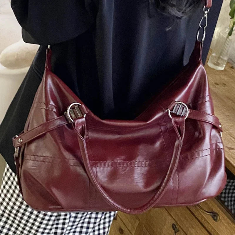 Sac à main en cuir bordeaux élégant avec bandoulière, détails en métal argenté, porté par une personne en tenue noire et blanche. Accessoire mode chic.