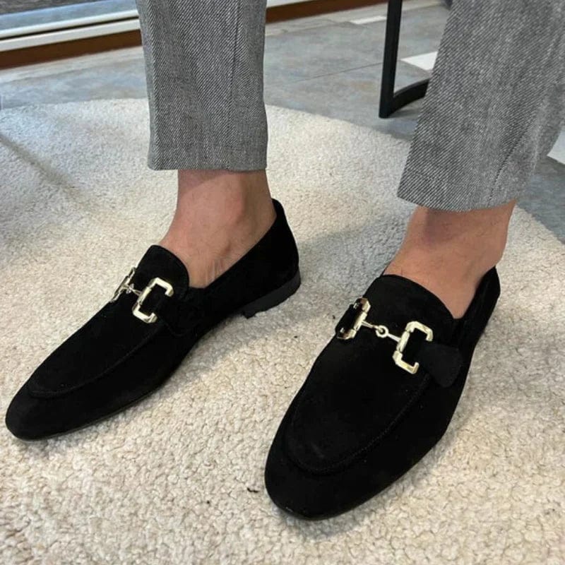 Chaussures mocassins noires élégantes avec boucle dorée, portées avec un pantalon gris. Mode masculine, style chic et moderne.