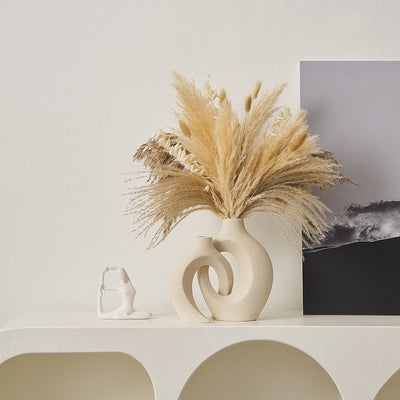 Vase moderne en céramique beige avec herbes de pampa séchées, posé sur une étagère blanche, à côté d'une petite sculpture abstraite.