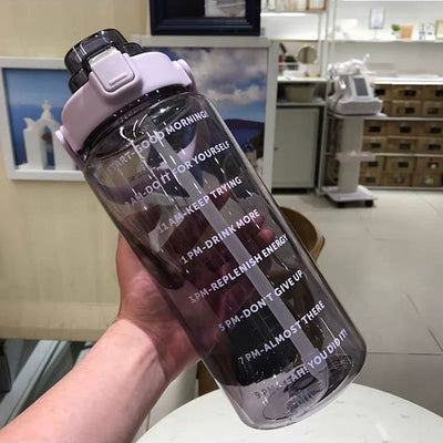 Bouteille d'eau transparente avec marquages horaires motivants, bouchon blanc, tenue en main. Accessoire fitness, hydratation quotidienne.