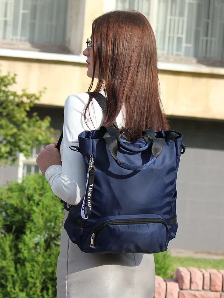 Femme portant un sac à dos bleu élégant en tissu imperméable, idéal pour le voyage et le quotidien, devant un bâtiment moderne.