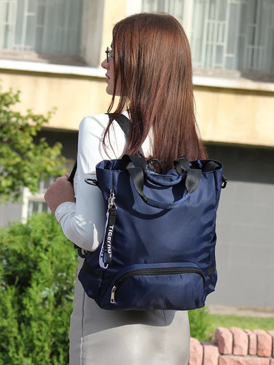 Femme portant un sac à dos bleu élégant en tissu imperméable, idéal pour le voyage et le quotidien, devant un bâtiment moderne.