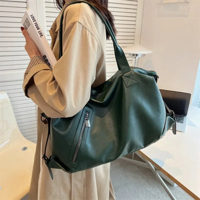 Femme portant un grand sac à main vert en cuir, tenant un livre, vêtue d'un manteau beige. Accessoire mode tendance, style élégant et moderne.