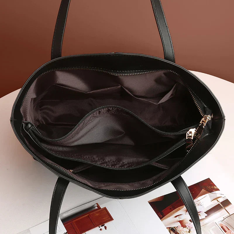 Sac à main noir ouvert avec doublure intérieure marron, compartiments zippés, sur une table blanche. Accessoire mode femme élégant et pratique.