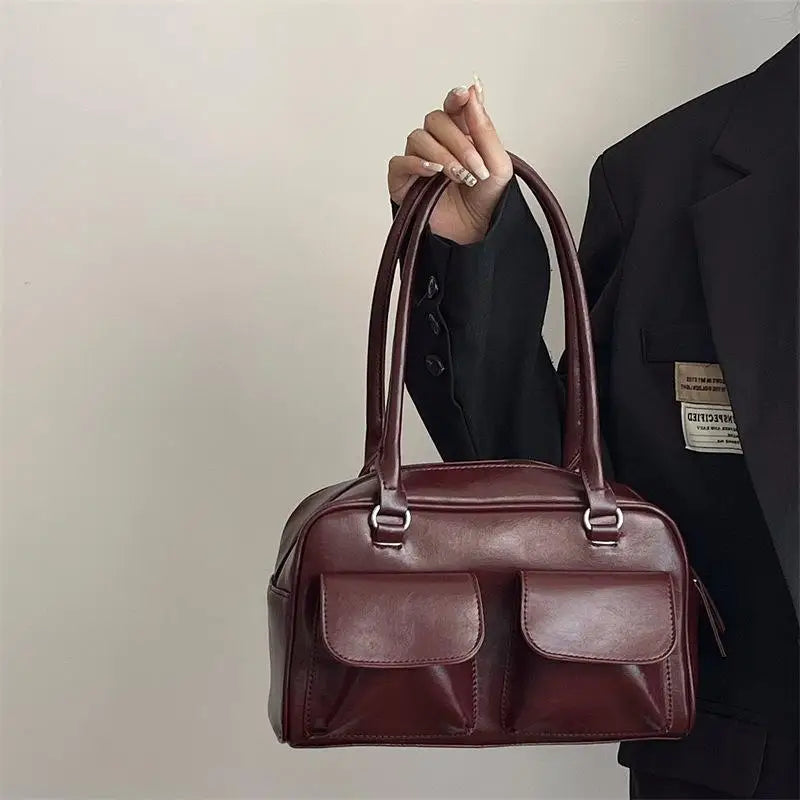 Sac à main en cuir marron avec deux poches avant, porté par une personne en veste noire. Accessoire mode élégant et tendance.