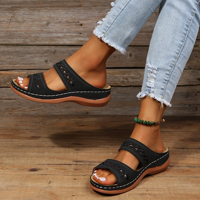 Sandales noires en cuir avec semelle marron, portées avec un jean déchiré. Accessoire de cheville vert. Mode estivale décontractée.