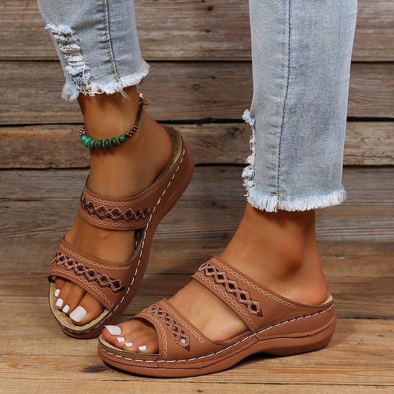 Sandales marron en cuir avec motifs ajourés portées avec un jean déchiré. Accessoire de cheville en perles vertes. Mode estivale décontractée.