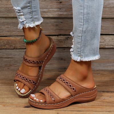 Sandales marron en cuir avec motifs ajourés portées avec un jean déchiré. Accessoire de cheville en perles vertes. Mode estivale décontractée.