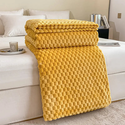 Couverture en peluche jaune texturée sur un lit blanc, avec oreillers blancs et une table de chevet moderne. Décoration chambre cosy et élégante.