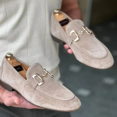 Homme tenant des mocassins en daim beige avec boucle métallique, mode élégante pour hommes, chaussures de luxe, style décontracté chic.
