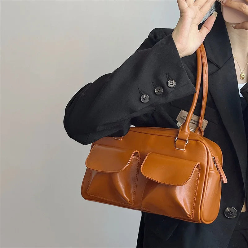 Sac à main en cuir marron avec poches avant, porté par une personne en veste noire. Accessoire mode élégant et tendance pour femmes.