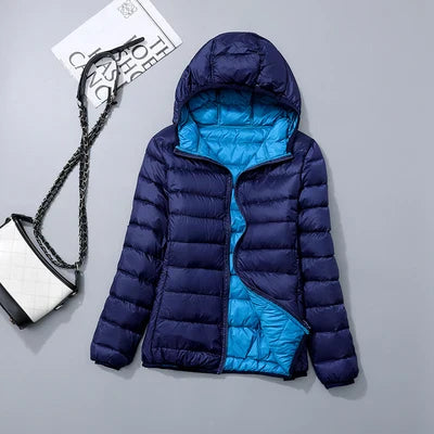 Doudoune bleue à capuche pour femme, doublure turquoise, posée à plat avec sac à main blanc et noir en arrière-plan. Mode hiver tendance.