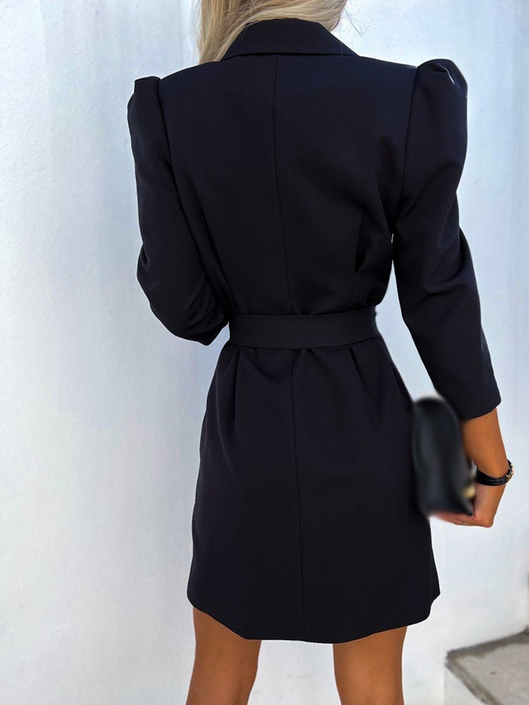 Robe blazer noire élégante pour femme, manches longues, ceinture à la taille, style chic et moderne, fond blanc minimaliste.