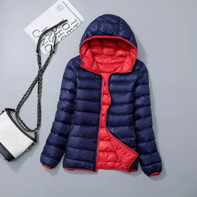 Doudoune réversible bleu marine et rouge avec capuche, posée à plat. Sac à main blanc avec chaîne noire à côté. Mode hiver, vêtements chauds.