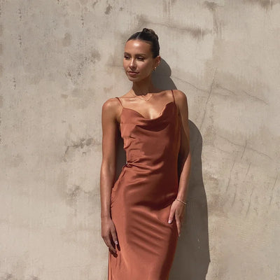 Femme en robe satinée orange, posant contre un mur texturé. Mode élégante, tenue chic, style estival.