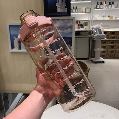 Bouteille d'eau transparente avec bouchon rose, inscriptions motivantes, tenue par une main dans un magasin moderne. Hydratation, motivation, design.