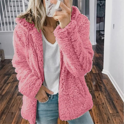 Femme portant un manteau en fausse fourrure rose, tenue décontractée avec jean et t-shirt blanc, mode automne-hiver, intérieur maison.