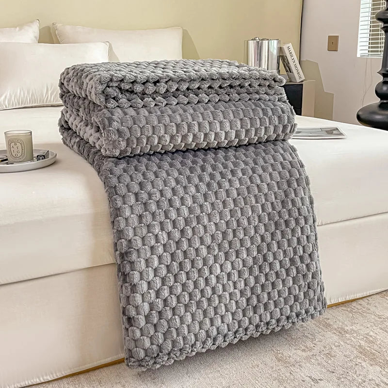 Couverture en tricot gris texturé posée sur un lit blanc, décor moderne. Accessoires de chambre élégants, ambiance cosy et chaleureuse.