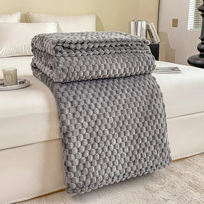 Couverture en tricot gris texturé posée sur un lit blanc, décor moderne. Accessoires de chambre élégants, ambiance cosy et chaleureuse.
