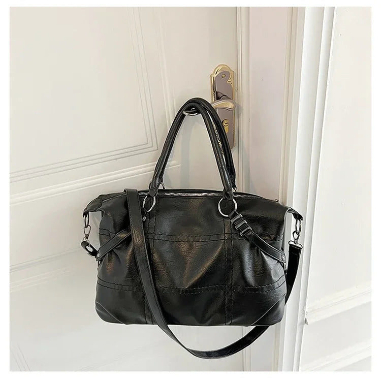 Sac à main noir en cuir suspendu à une poignée de porte, design élégant avec bandoulière, idéal pour mode féminine et accessoires tendance.
