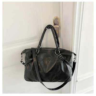Sac à main noir en cuir suspendu à une poignée de porte, design élégant avec bandoulière, idéal pour mode féminine et accessoires tendance.