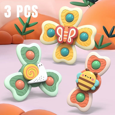 Trois jouets fidget spinner colorés en forme de papillon, escargot et abeille, sur fond pastel avec plantes. Jouets anti-stress pour enfants.