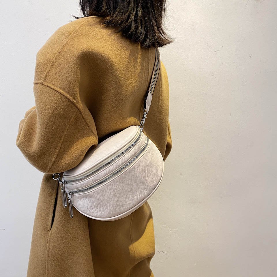 Femme portant un manteau camel avec un sac banane blanc en cuir, style moderne et minimaliste, mode automne-hiver, accessoires tendance.