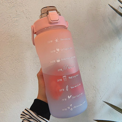Bouteille d'eau graduée rose avec couvercle, motifs inspirants, tenue par une main. Accessoire fitness, hydratation quotidienne.